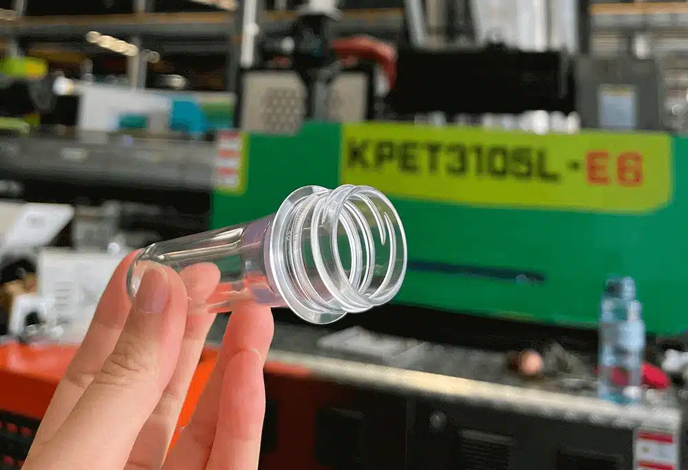 Clear PET bottle preform with threaded neck held by hand in front of molding machine