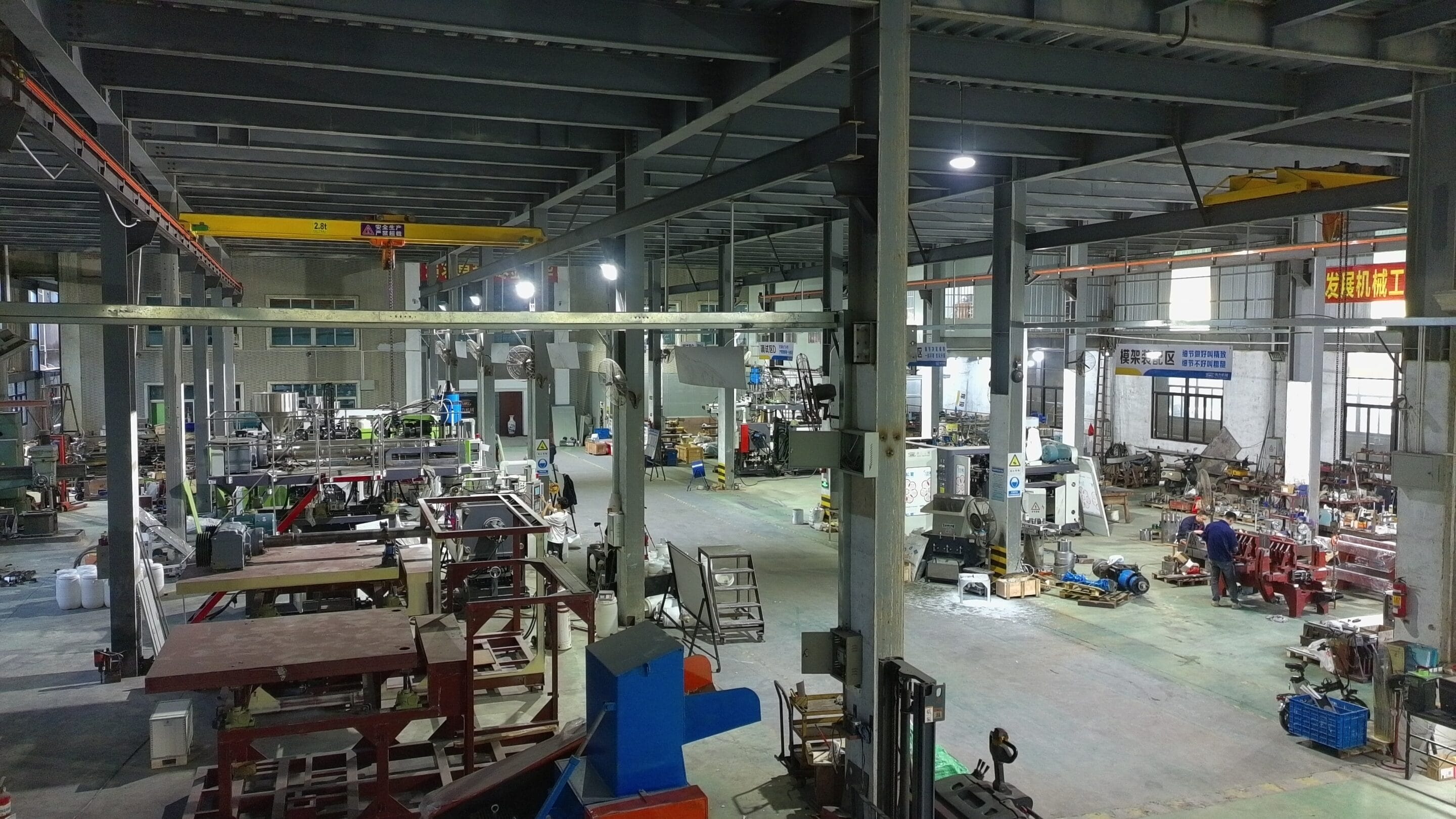 Extrusion blow molding machine factory workshop with assembled frames, overhead crane and technicians on shop floor