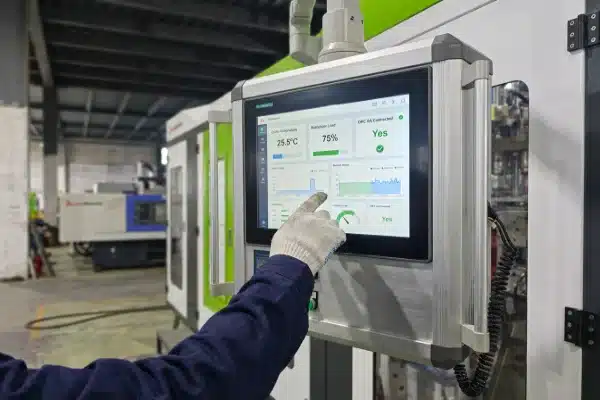 A close-up of an operator using a modern HMI touch screen on an all-electric blow molding machine to monitor integrated production line data and auxiliary equipment performance.