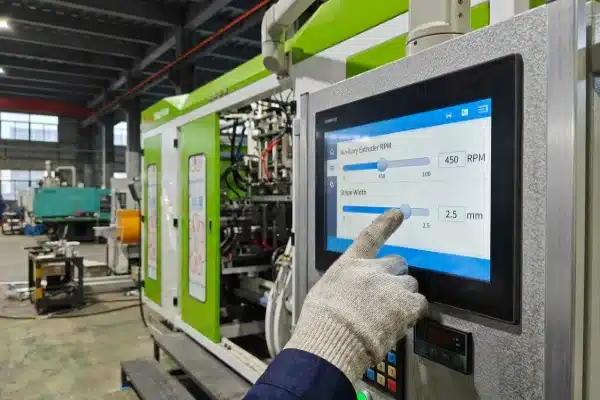 A first-person perspective of a hand adjusting auxiliary extruder RPM and stripe width parameters on a high-tech HMI touchscreen panel of a LEKA all-electric blow molding machine.